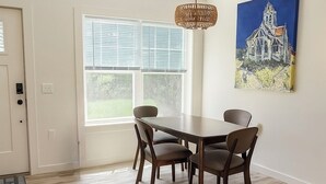 Ein Essbereich mit Holztisch und Stühlen, einer Pendelleuchte und einem großen Fenster mit Jalousien.