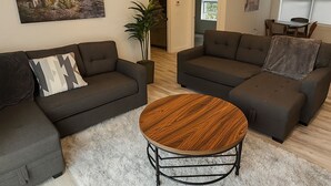 Ein modernes Wohnzimmer mit zwei Sofas, einem runden Couchtisch und einem Gemälde von einem Leuchtturm.