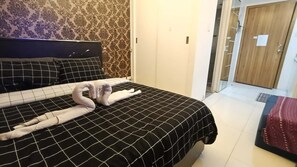 A hotel room with a bed, a headboard, a patterned wall, and a door. - Grand Riviera Condotel Near St Lukes Medical Center (Manila)