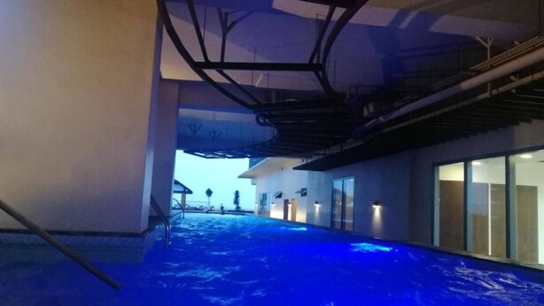 An indoor swimming pool with a blue-lit floor, a staircase, and a view of the outside. - Grand Riviera Condotel Near St Lukes Medical Center (Manila)