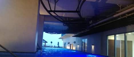 An indoor swimming pool with a blue-lit floor, a staircase, and a view of the outside.