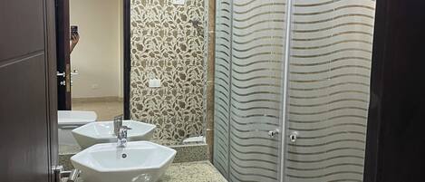 A bathroom with a shower, two sinks, a toilet, and a mirror.