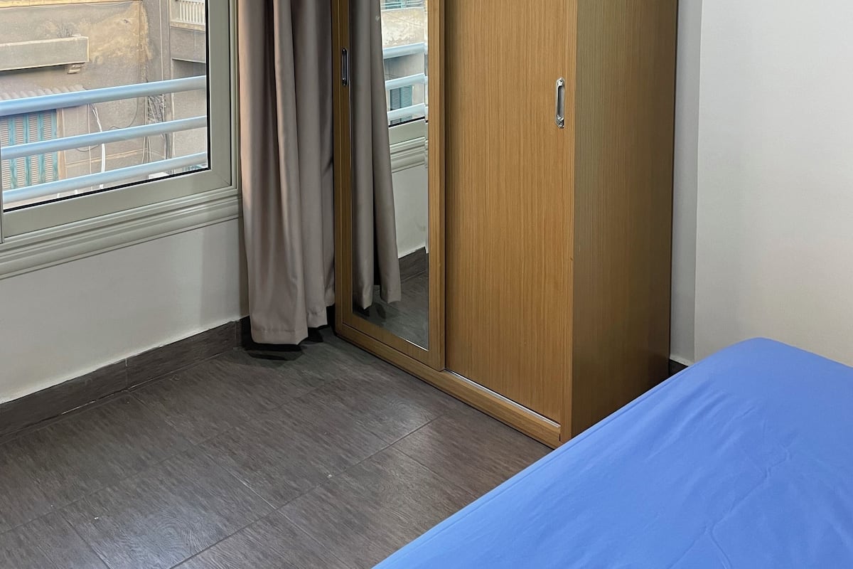 A bedroom with a large window, a wardrobe, and a bed.