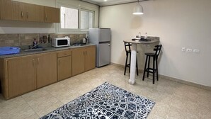 A compact kitchen with wooden cabinets, a refrigerator, a microwave, and a small dining area with two stools. - Royal Residence Cairo (Giza)