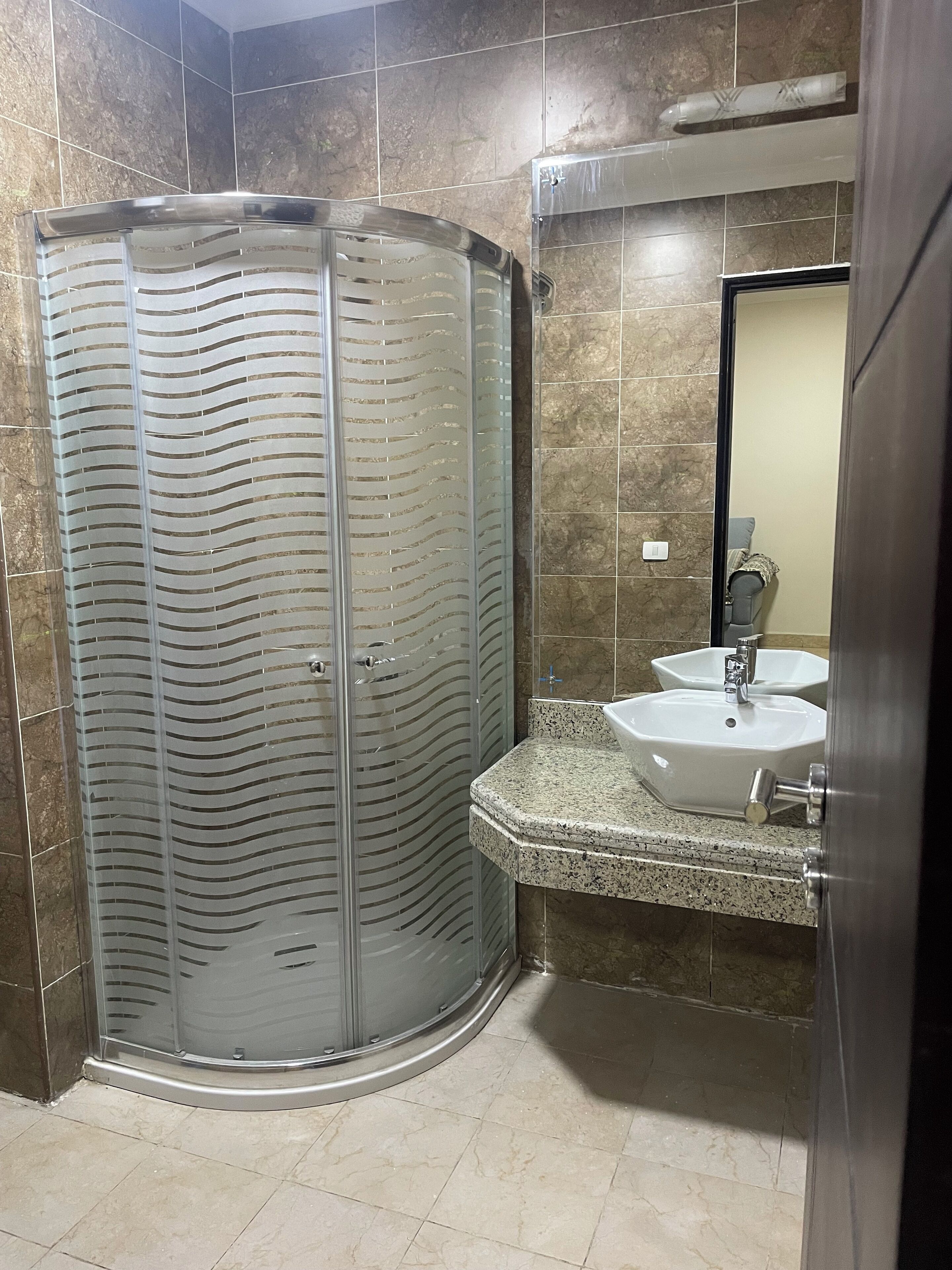 A modern bathroom with a glass-enclosed shower, a granite countertop, and a white sink.