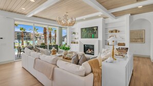 Una sala de estar moderna con un sofá blanco, una chimenea y vistas a palmeras afuera.
