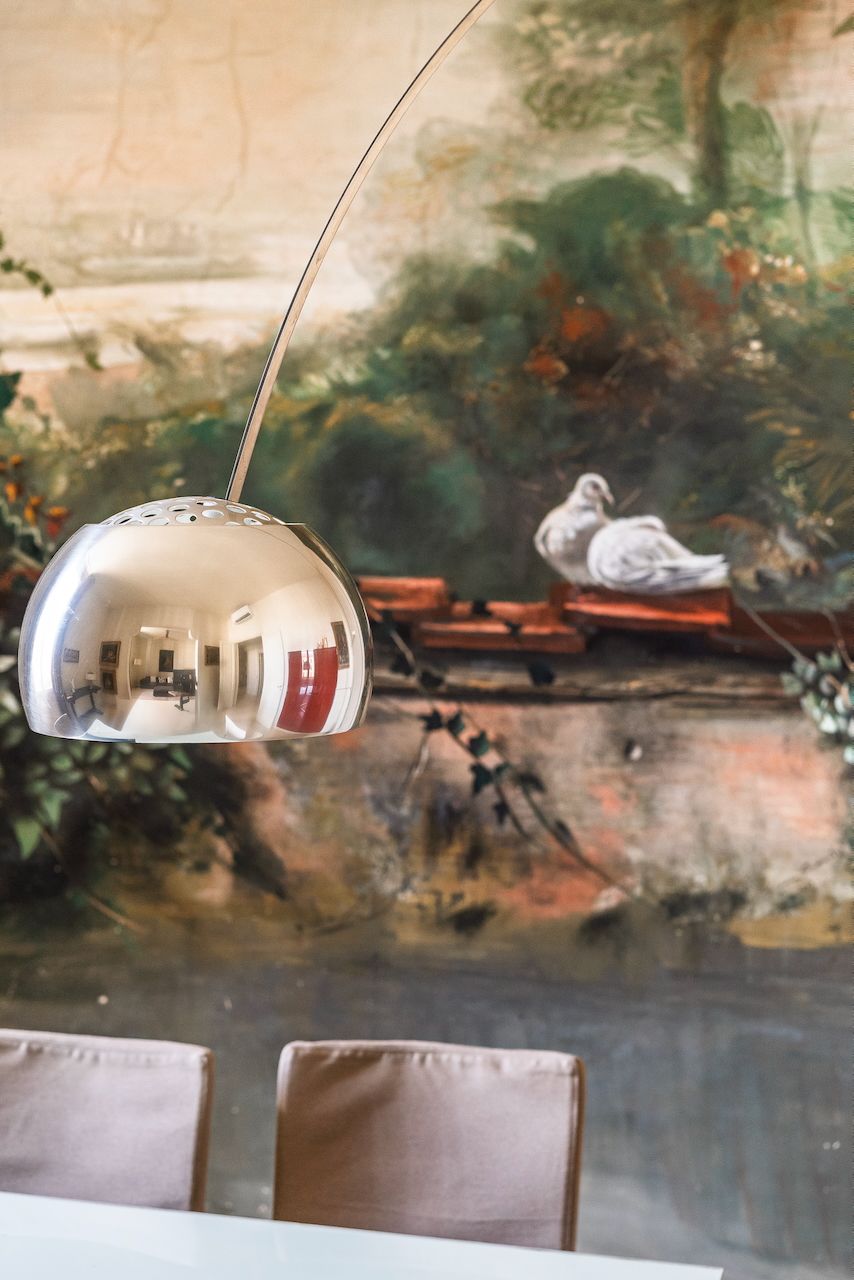 Zona pranzo con lampada a sospensione moderna, un murale con uccelli e vegetazione, e un tavolo con sedie.