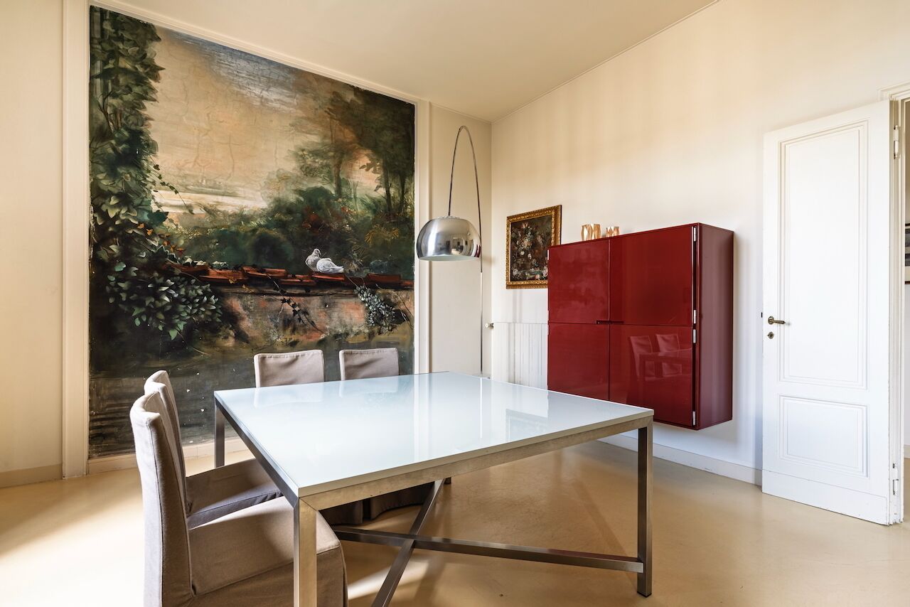 Un comedor con una mesa y sillas blancas, un armario rojo y un cuadro grande con un paisaje en la pared.