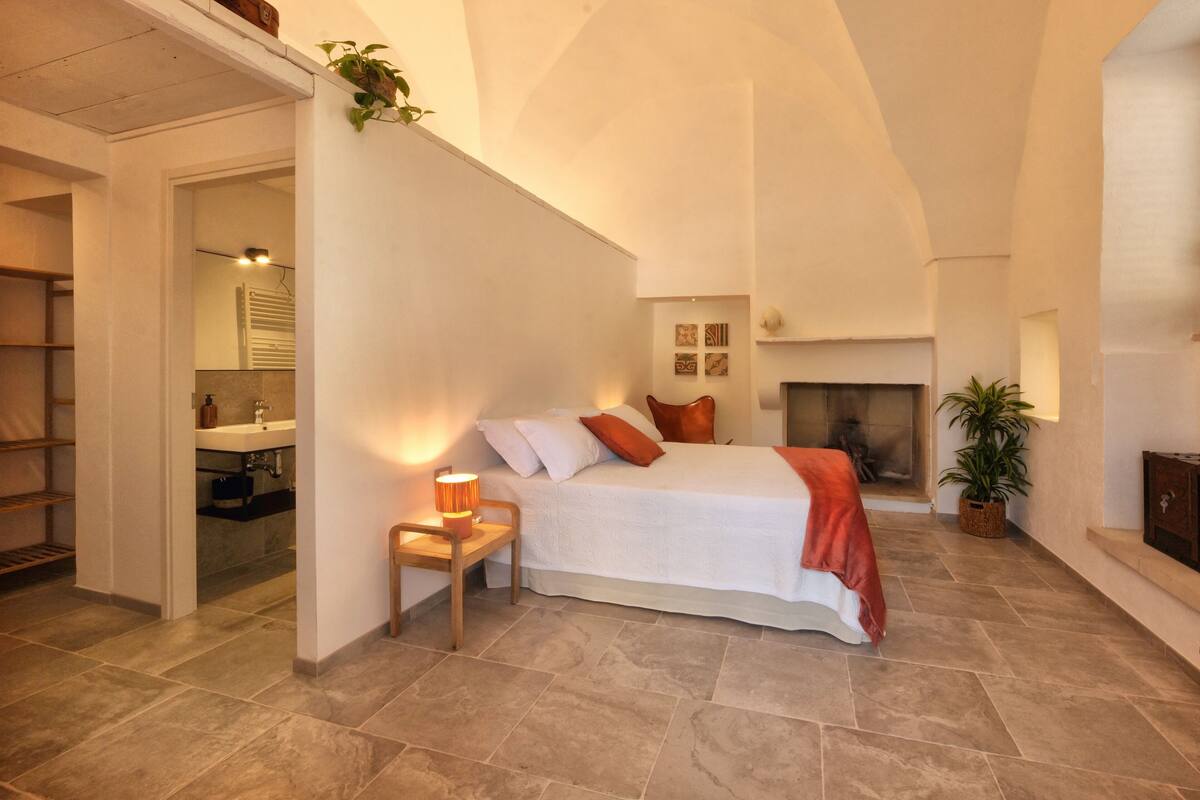 Quarto com cama, mesa de cabeceira e lareira.