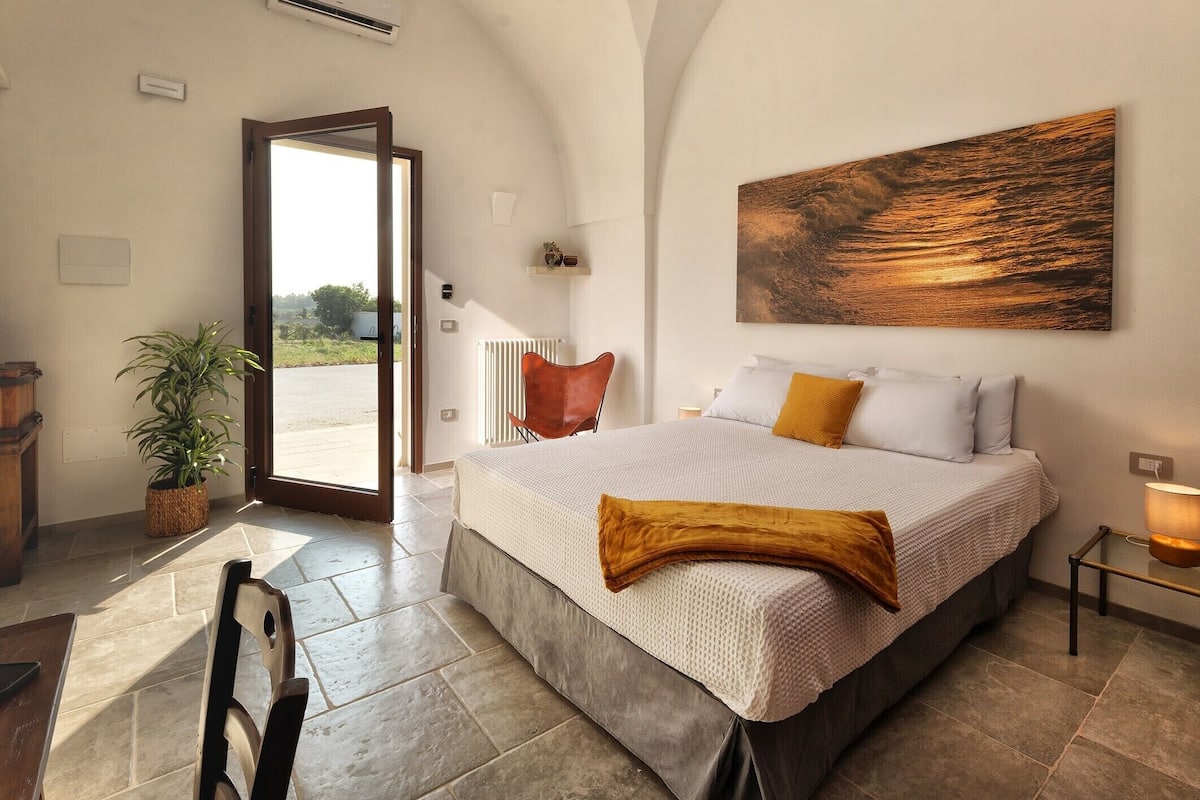 Quarto com uma cama grande, uma planta em vaso, uma cadeira e um quadro na parede.