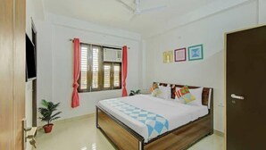 Une chambre à coucher avec un lit, un ventilateur de plafond, une fenêtre avec des rideaux, une plante en pot et une porte.