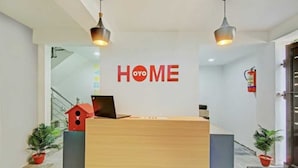 Un comptoir d’accueil avec un plan de travail en bois et un ordinateur portable, une boîte aux lettres rouge et une pancarte « ENTRÉE » sur le mur.
