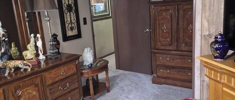 A room with a wooden dresser, a mirror, a lamp, a small table, and a television.