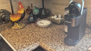 A kitchen with dark cabinets, a coffee maker, a rooster decoration, and a kettle on the counter.