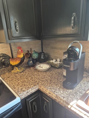 A kitchen with dark cabinets, a coffee maker, a rooster decoration, and a kettle on the counter. - Ideal for traveling professionals. Private 2-bedroom home in peaceful Mansfield. (Mansfield)