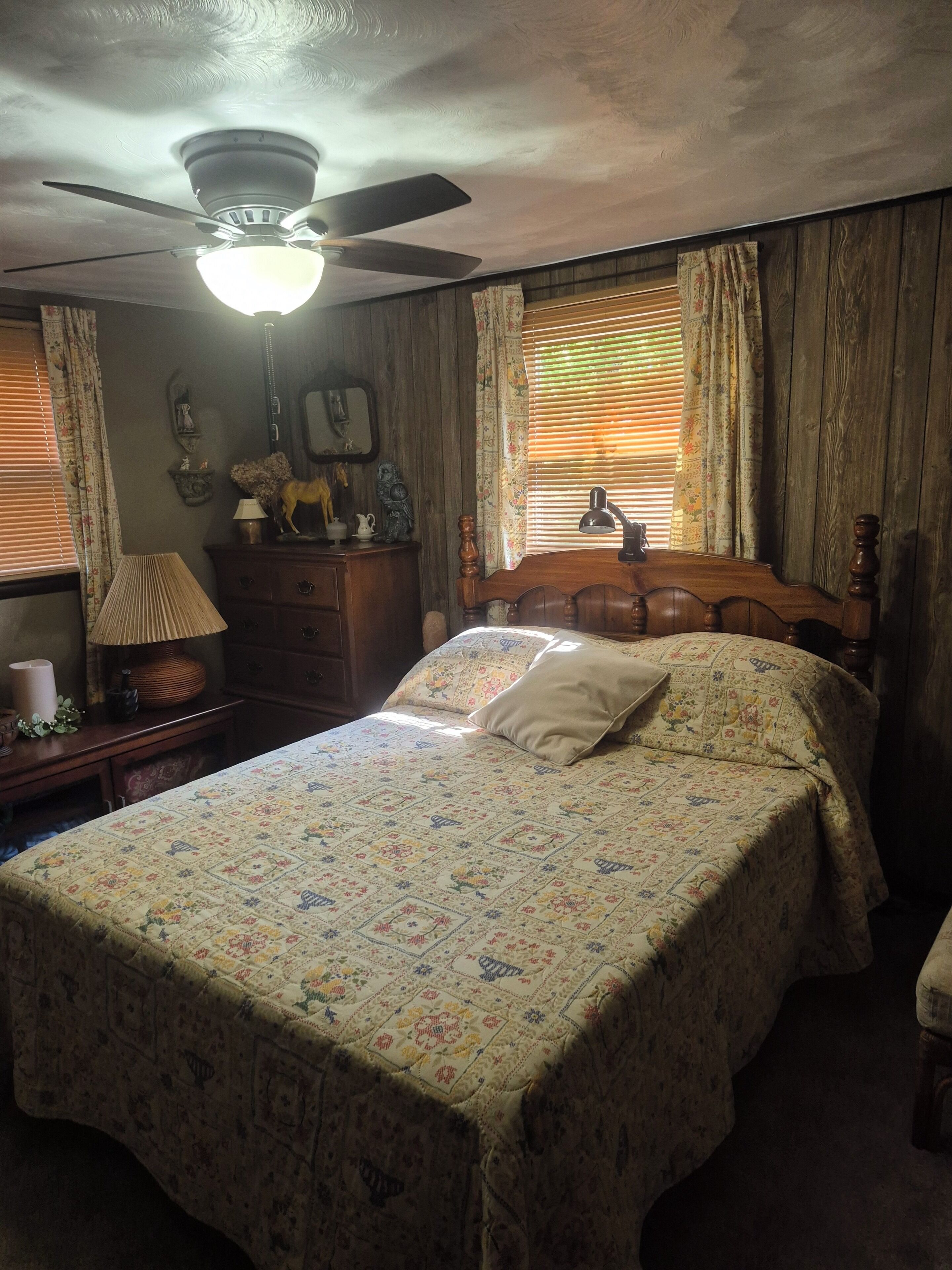A bedroom with a bed, a ceiling fan, a dresser, a lamp, and curtains.