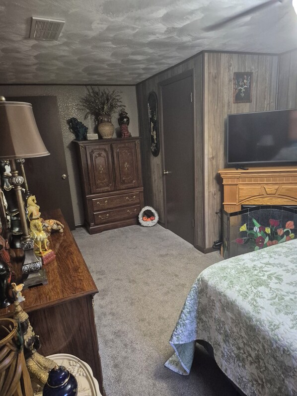 Un dormitorio con cama, cómoda, lámpara y televisor sobre un mueble.