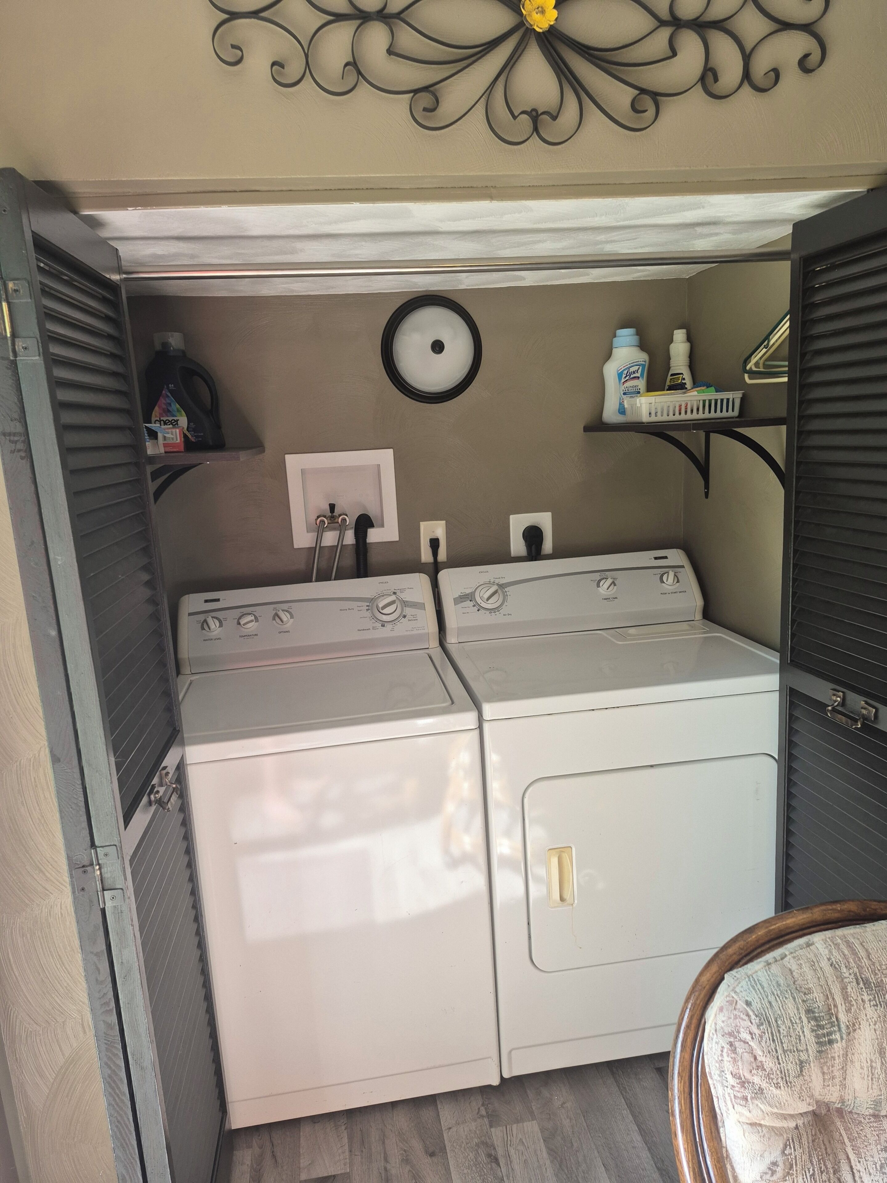 A laundry room with two stacked washers and dryers, a wall-mounted light fixture, and a shelf with cleaning supplies.