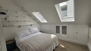 A bedroom with a bed, a skylight, built-in wardrobes, and a small round stool.
