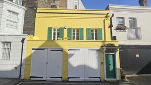 A yellow building with green shutters, a green door, and two white garage doors.