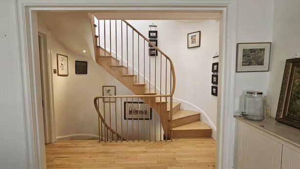 A wooden staircase with a curved design, white walls, and framed pictures on the walls.