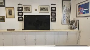 A room with a large flat-screen TV mounted on a wall, surrounded by framed pictures and artwork.
