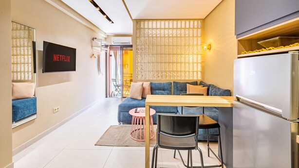 Une cuisine moderne dotée d’un réfrigérateur encastré, un coin repas avec une table et des chaises, un canapé bleu et un téléviseur fixé au mur qui affiche « NETFLIX ».