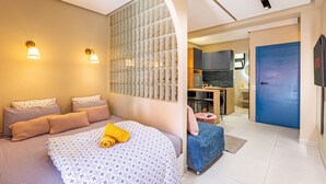 Une chambre d’hôtel moderne avec un grand lit, une kitchenette, une porte bleue et un téléviseur fixé au mur.