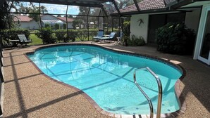 A swimming pool with a glass enclosure, surrounded by a pebble deck and a covered patio area with lounge chairs.