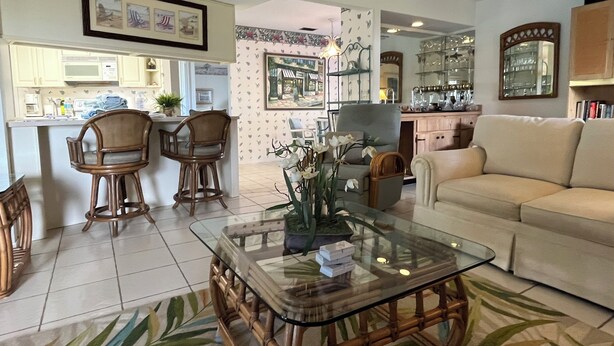 A spacious living room with a glass coffee table, a beige sofa, and a dining area with wooden chairs and a kitchen in the background.