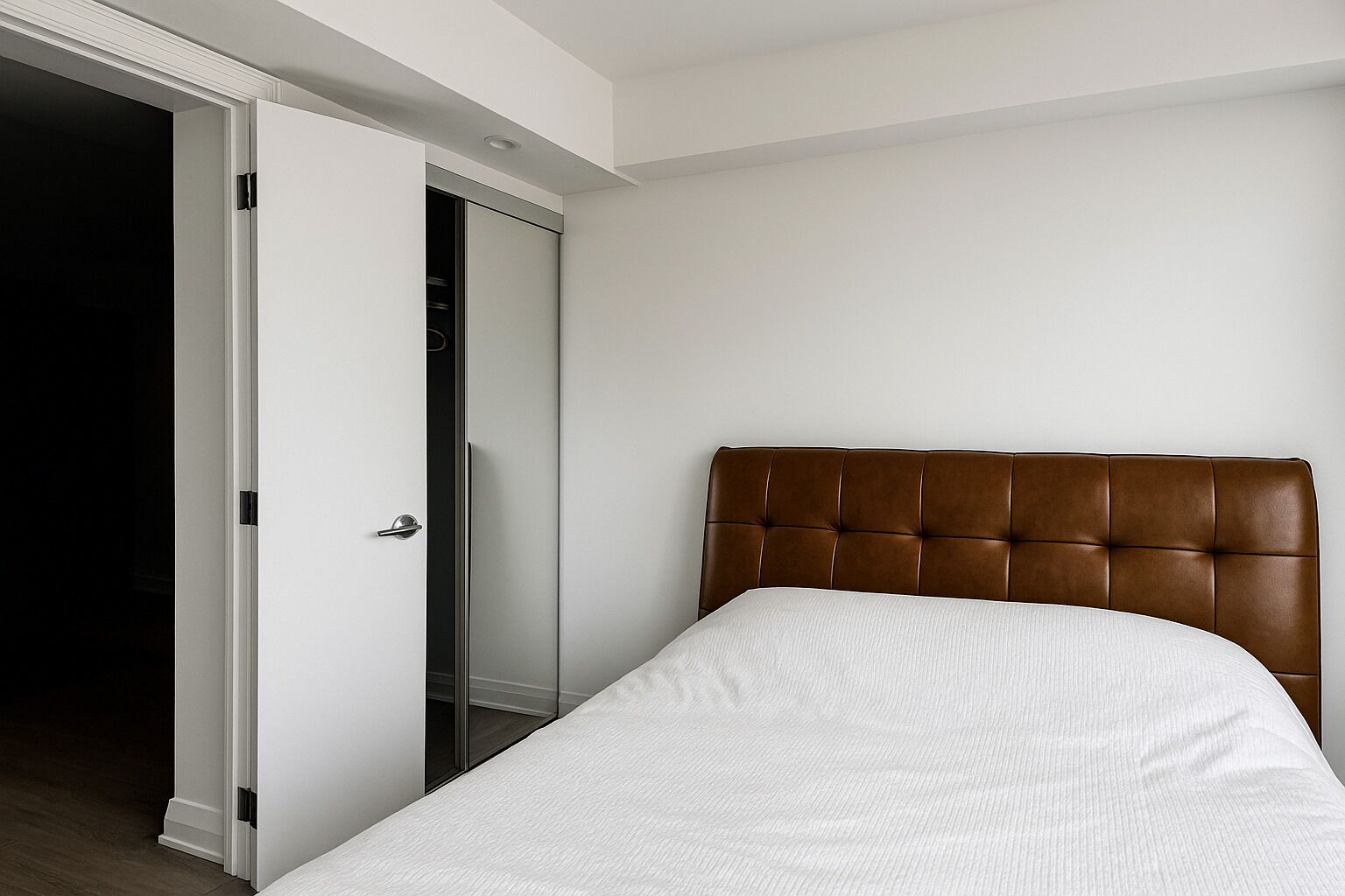 A bedroom with a bed, a brown headboard, and a white door leading to a closet.