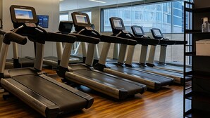 A gym with multiple treadmills, a wooden floor, and a large window providing a view of the city.