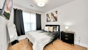 Une chambre à coucher comprenant un lit, une table de chevet, un miroir et un téléviseur fixé au mur.
