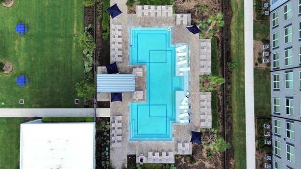 Vue aérienne d’un espace piscine doté de plusieurs chaises longues et de parasols, entouré de verdure et jouxtant un bâtiment.