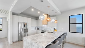 A modern kitchen with a marble island, stainless steel appliances, and pendant lighting. - Stylish Oceanview Kayak Getaway w/ Pool & Hot Tub! (Key Largo)