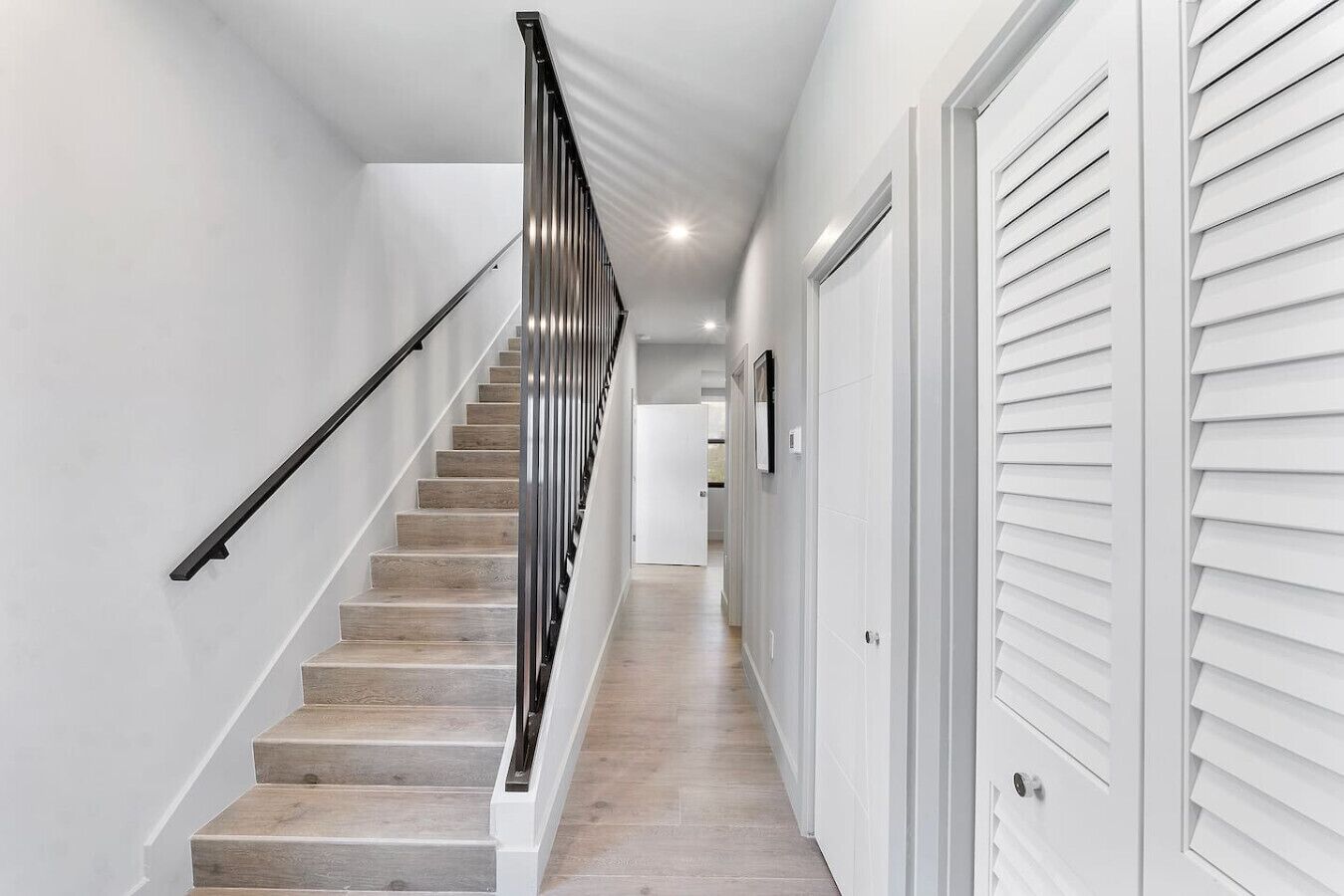 A modern staircase with a metal handrail, wooden steps, and white walls.