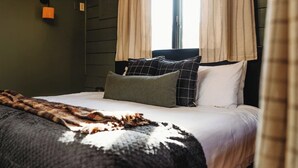 Una cama con una manta estampada, dos almohadas y una lámpara fijada a la pared.