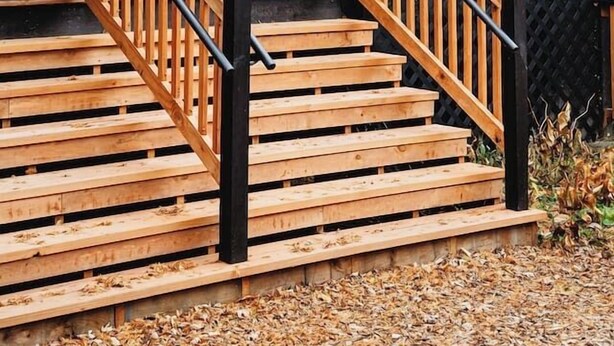 Una cabaña de madera con una escalera y una puerta negra.