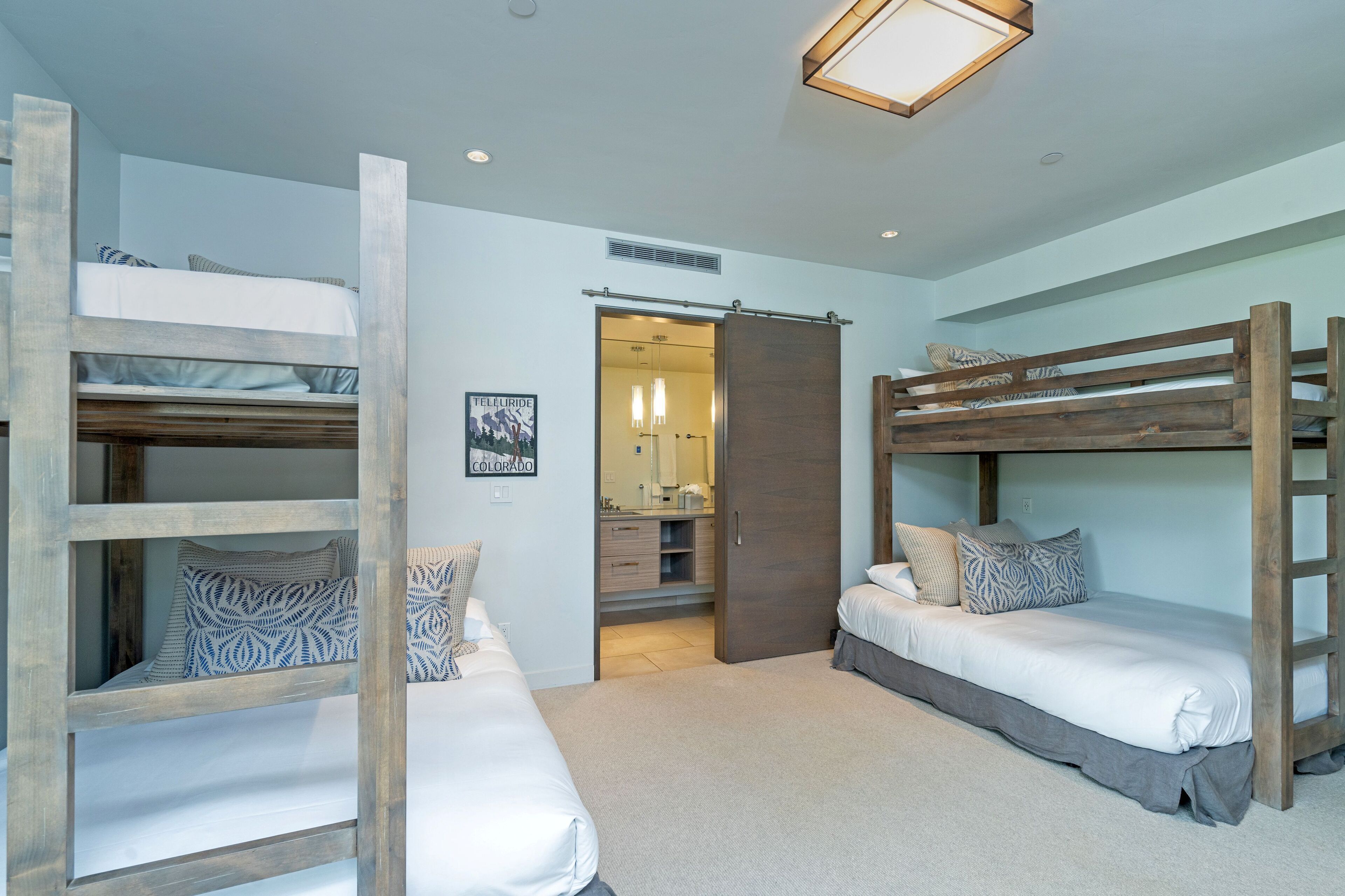 A bedroom with two bunk beds, a bathroom with a mirror, and a door leading to another room.