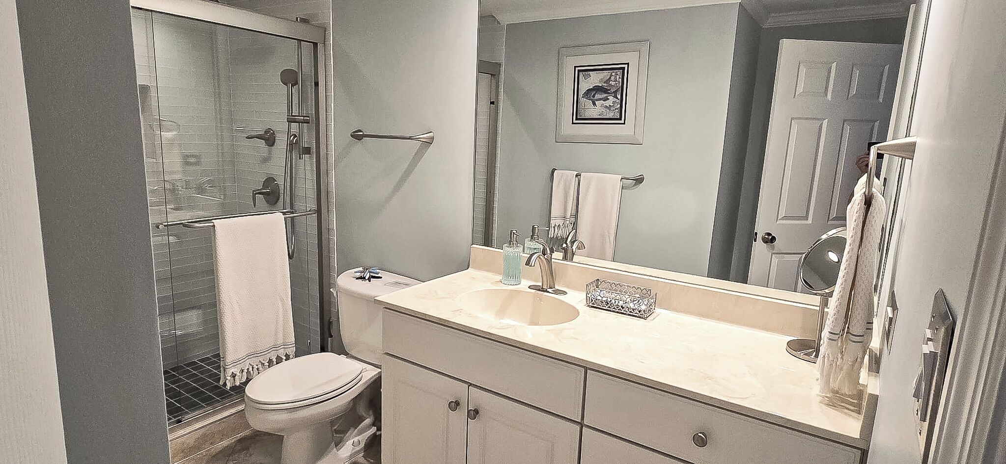 Un baño con cabina de ducha de vidrio, inodoro, lavabo con espejo y perchero para toallas.