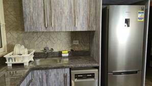 A kitchen with wooden cabinets, a stainless steel refrigerator, and a dishwasher. - Madinaty Botanic Bliss (Cairo Governorate)