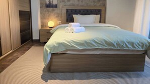 A neatly made bed with a light green bedspread and two rolled towels, a bedside lamp, and a framed picture on the wall. - Madinaty Botanic Bliss (Cairo Governorate)