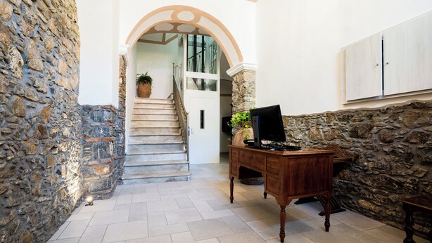 A hallway with stone walls, a wooden desk, and a staircase leading to an upper level. - Harmonia home (Capitello)