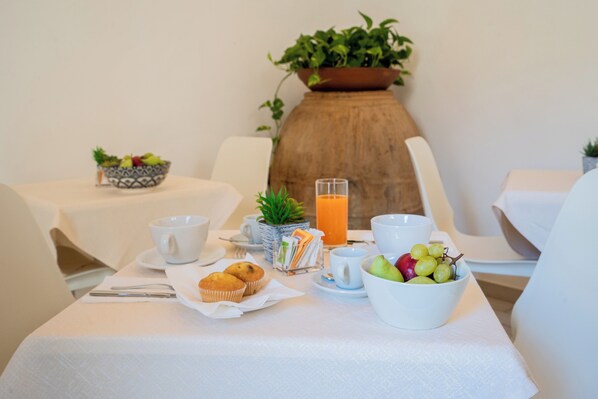 A breakfast setup with a bowl of fruit, muffins, a glass of orange juice, and a cup on a table. - Harmonia home (Capitello)