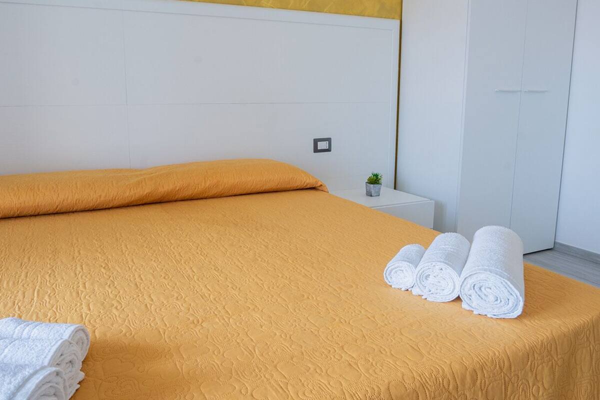 A hotel room with a bed, a nightstand, a small potted plant, and a door.