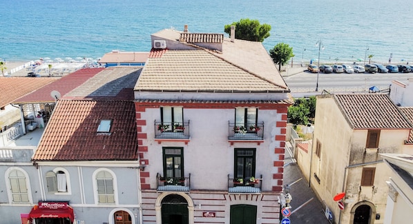 A building with a tiled roof, a balcony with flowers, and a view of the sea.