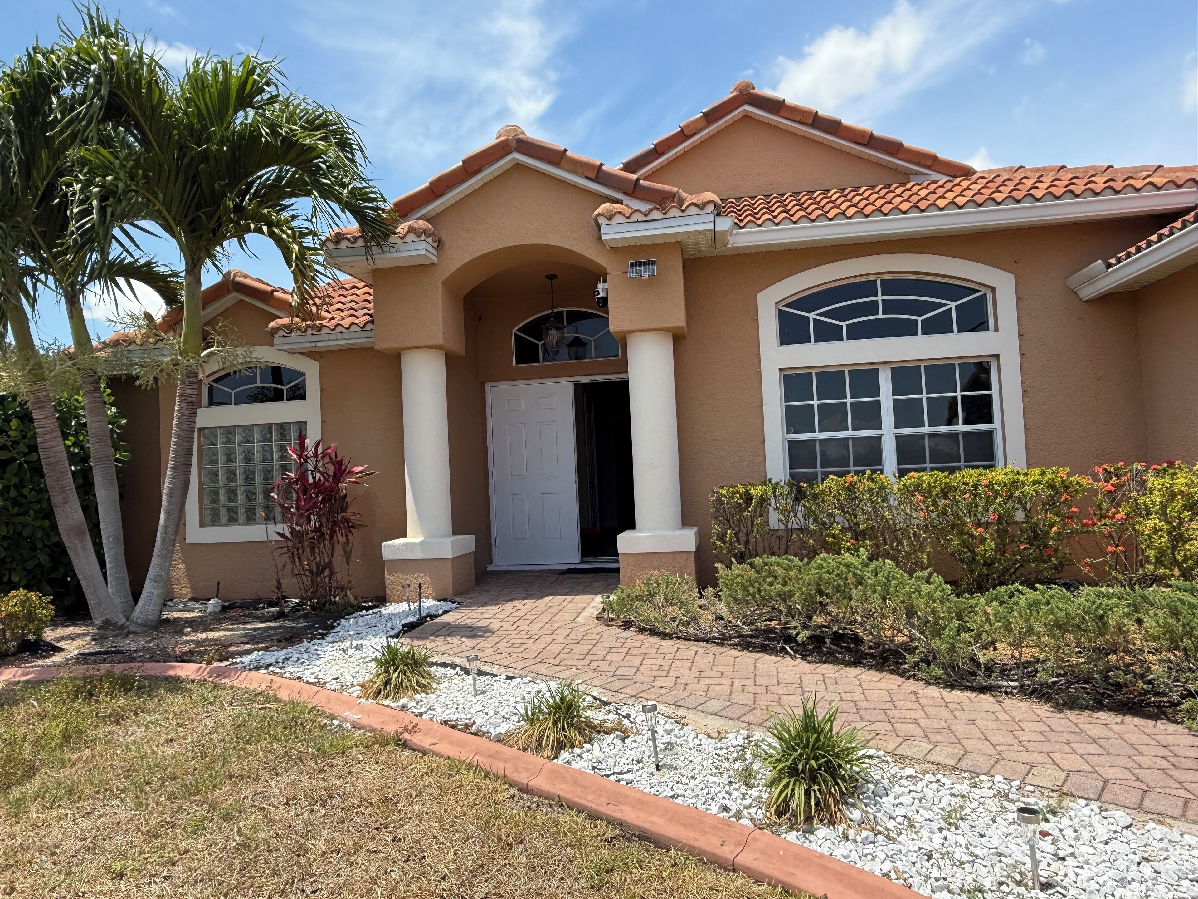 A two-story house with a beige facade, red-tiled roof, and a central entrance with a white door.