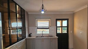 Een moderne keuken met een inbouwkookeiland, een raam met zonwering, en een deur met glaspanelen.