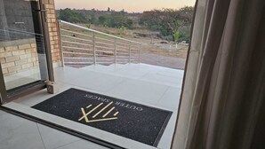 Een hotelentree met een zwarte deurmat waarop 'XVI HOTEL' staat en een uitzicht op een aangelegde tuin met een metalen hekwerk.