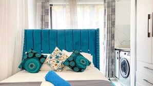 A neatly made bed with a teal headboard, two decorative pillows, and a rolled towel. - Pazoori Stays at SmartHomes (Nairobi)